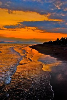 an orange and blue sunset over the ocean with people walking on the beach in the distance