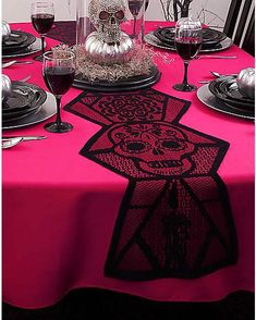 a table topped with plates and glasses filled with red wine next to a skull head