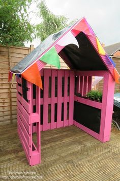 a pink play house with a black roof and colorful flags on it's side