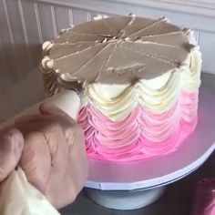 a person is decorating a cake with pink and white icing