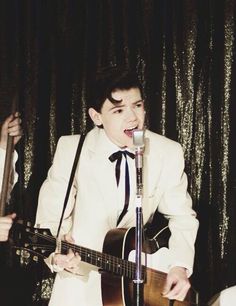 a man in a white suit singing into a microphone while holding a guitar and standing next to him