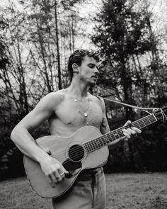 a shirtless man holding an acoustic guitar