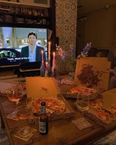 pizzas and wine are sitting on the table in front of a flat screen tv