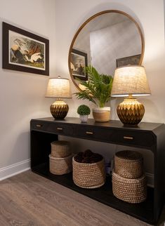 a table with two lamps and baskets on it in front of a large round mirror