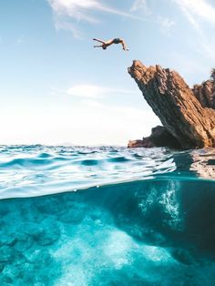 a person jumping off a cliff into the ocean from an island in the middle of the ocean