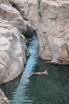 there is a man swimming in the water next to some large rocks and rock formations