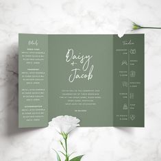 a green and white wedding program booklet with flowers on it, sitting next to a flower vase