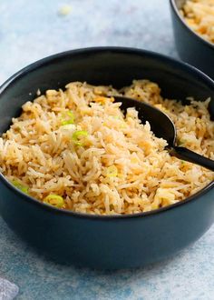 two black bowls filled with rice on top of a blue tablecloth and one has a spoon in it