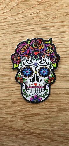 a sticker with a sugar skull and roses on it's head, sitting on top of a wooden surface