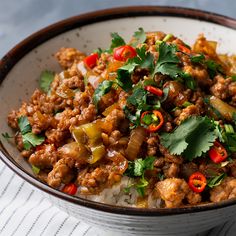 a white bowl filled with rice and meat covered in cilantro, red peppers and green onions