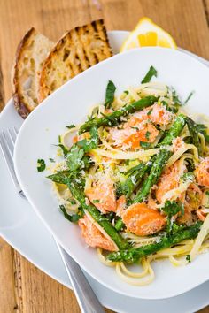 a white plate topped with pasta covered in shrimp and veggies next to slices of bread