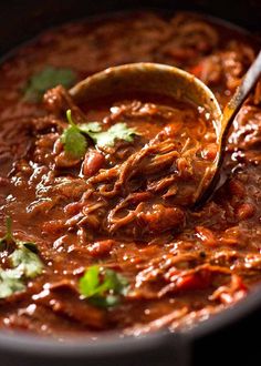 a spoon full of chili with meat and cilantro on the side in a black pot