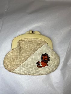 a small purse with a lion embroidered on the front and side, sitting on top of a white sheet