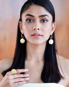 a woman with long black hair wearing gold earrings and blue eyeshadow is looking at the camera