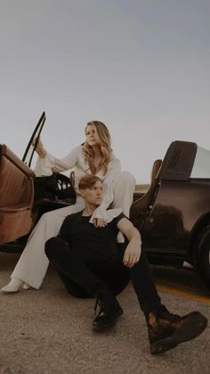 a woman sitting on the back of a car next to a man with a suitcase