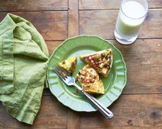 a green plate topped with slices of pizza next to a glass of milk and a napkin