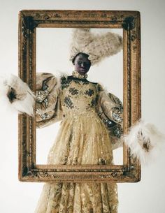 a woman is dressed in an elaborate dress and holding a frame with feathers on it