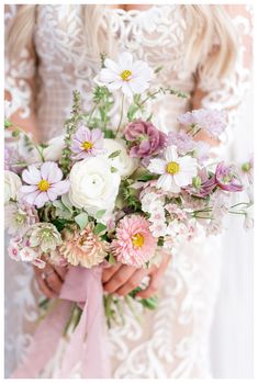 a bride holding a bouquet of flowers in her hands and wearing a wedding dress with lace