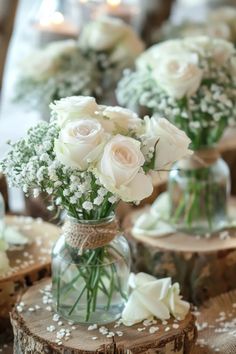 white roses are in a glass vase on top of a table with wood slices and candles