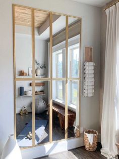 a large mirror sitting on top of a wooden floor next to a white curtained window