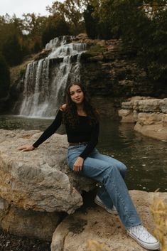 a woman sitting on top of a rock next to a waterfall