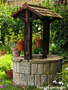 a small wooden gazebo in the middle of a garden with potted plants around it