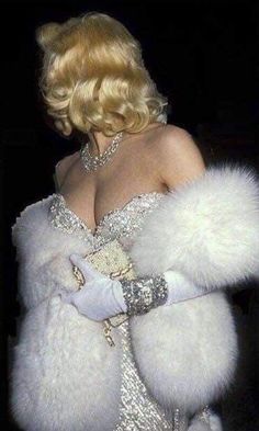 a woman in a white dress and fur stoler with her hands on her hips