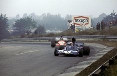 two racing cars driving down a road with people watching from the sidelines behind them