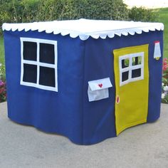 a blue and yellow play house sitting on top of a cement ground next to flowers