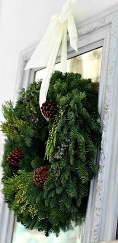 a wreath hanging from the side of a mirror with pine cones and evergreens on it