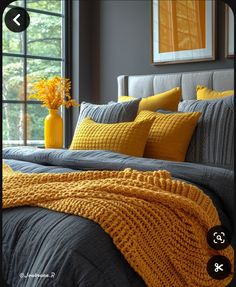 a bed with yellow pillows and blankets on top of it next to a large window