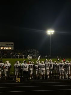 the football team is standing in a huddle on the sidelines at night time