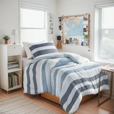 a bed with blue and white striped comforter in a bedroom next to two windows