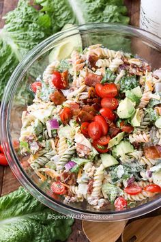 a salad in a glass bowl on top of a wooden cutting board next to lettuce and tomatoes