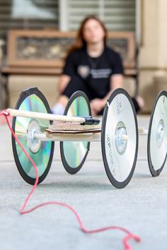 a woman sitting on a bench next to two wheels with cds attached to them,