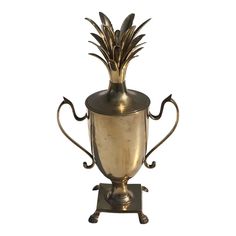 a brass vase with a pineapple on the top and two handles, sitting on a stand