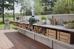 an outdoor bbq grill with lots of wood stacked on the counter and storage drawers