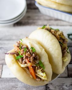 three tacos with meat and vegetables in them on a plate next to some plates