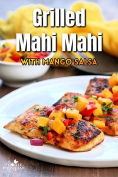 grilled mahi mahi with mango salsa on a white plate next to other food