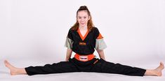 a woman sitting on the ground in a black and orange karate outfit with an orange belt