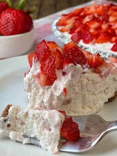 a slice of strawberry cream pie on a plate with a fork and bowl of strawberries in the background