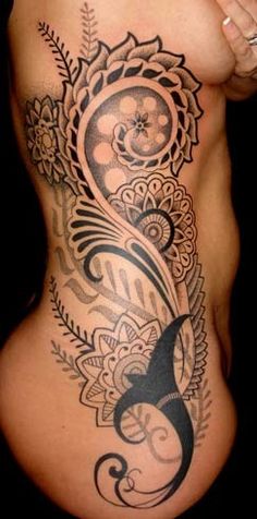 a woman's stomach with an intricate tattoo design on the side, and flowers