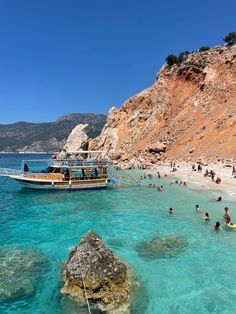 people are swimming in the clear blue water next to a rocky cliff and beach with a boat