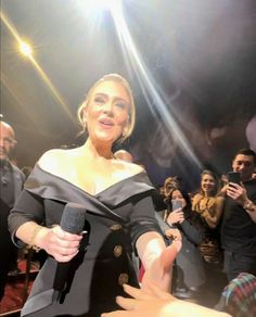 a woman in a black dress is holding a microphone and talking to someone on the red carpet