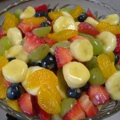 a fruit salad with bananas, oranges, grapes and strawberries in a glass bowl