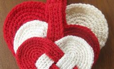 two red and white crocheted heart shaped dishcloths sitting on top of a wooden table