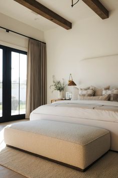 a large white bed sitting in a bedroom next to a sliding glass door and wooden beams