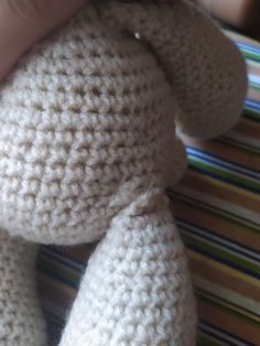 a crocheted teddy bear being held by someone's hand on a striped table cloth