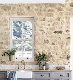 a kitchen with stone walls and gray cabinets in the corner, along with a window