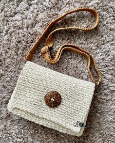 a crocheted white purse with a button on the front and strap around it